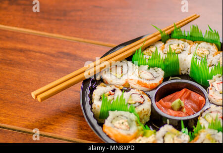 Close up d'un grand ensemble de délicieux rouleaux de sushi japonais sur une plaque en plastique noir sur une table en bois Banque D'Images