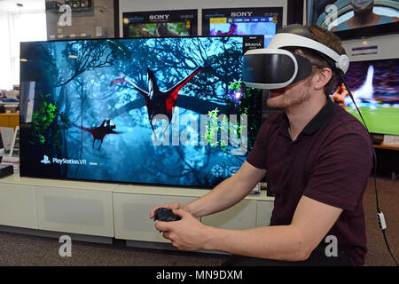 L'homme dans un magasin de détail portant un casque VR Sony Playstation avec contrôleur et jeu sur Sony TV Banque D'Images