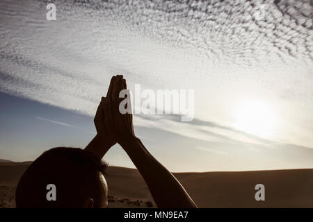 Closeup of a young caucasian man practicing yoga à l'extérieur, contre un ciel nuageux, avec le soleil en arrière-plan Banque D'Images