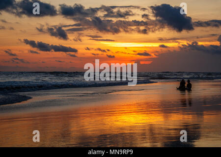 Plage de Berawa (Pantai Berawa) au coucher du soleil. Deux silhouettes de gens assis dans la marée. Canggu, Bali, Indonésie. Banque D'Images