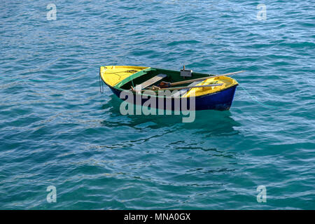 Petit bateau à rames et avirons colorés amarrés dans l'eau bleue et claire de l'océan Atlantique avec une réflexion sur les vagues et ondulations. Banque D'Images