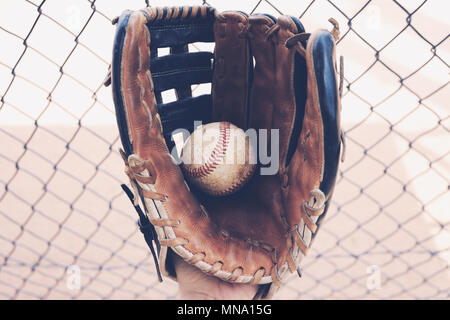 Le sport américain de baseball balle de gros plan montre dans la main à partir de la fosse. Domaine en arrière-plan de clôture, super pour les sports graphique. Banque D'Images