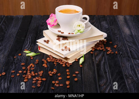 Cop de café sur le dessus de la pile de livres avec des grains de café et fleurs éparpillées sur la table Banque D'Images