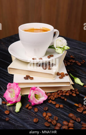 Cop de café sur le dessus de la pile de livres avec des grains de café et fleurs éparpillées sur la table Banque D'Images