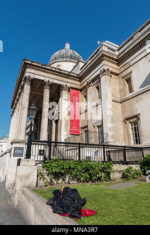 Une personne sans-abri dans le centre de londres endormi dans un sac de couchage sur l'herbe de la pelouse ou à l'extérieur de la National Gallery à Trafalgar Square à Londres. Banque D'Images