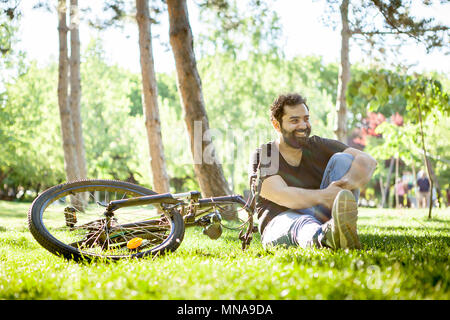 Jeune homme barbu sourit à la caméra assis sur le sol dans l'herbe Banque D'Images