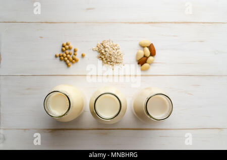 Passage tiré du soja, l'avoine et le lait d'amande des boissons dans une rangée de bouteilles ouvertes avec des ingrédients sur les planches de bois peintes en blanc, table. Peu de profondeur d'Epe Banque D'Images