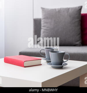 Close up of book et deux tasses se trouvant sur une petite table, canapé et une lampe à l'arrière-plan. Banque D'Images