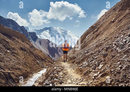 Randonneur dans une chemise orange avec sac à dos marche sur le sentier au sommet enneigé en arrière-plan Banque D'Images