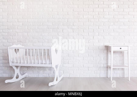 Berceau en bois blanc, et petite table debout à la lumière intérieur avec mur de brique décorative Banque D'Images