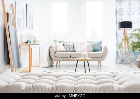 Matelas gris et échelle en salon lumineux avec canapé beige, table et lampe Banque D'Images