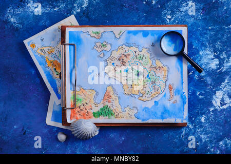 Voyages en mer et la peinture concept. Fantasy aquarelle carte sur un presse-papiers en bois avec une loupe sur un fond bleu marine avec l'exemplaire de l'espace. Banque D'Images