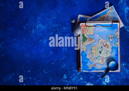 Voyages en mer et la peinture concept. Fantasy aquarelle carte sur un presse-papiers en bois avec une loupe sur un fond bleu marine avec l'exemplaire de l'espace. Banque D'Images