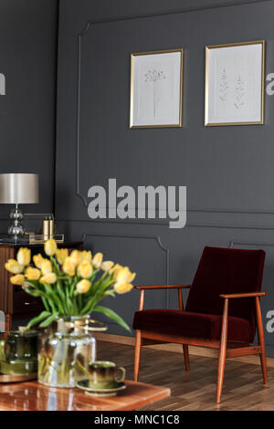 Tulipes jaune floue sur table en bois en rétro salon intérieur avec des affiches ci-dessus fauteuil Banque D'Images