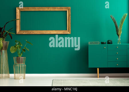 Les plantes fraîches placés dans le salon intérieur avec placard vert et or châssis maquette accroché au mur Banque D'Images