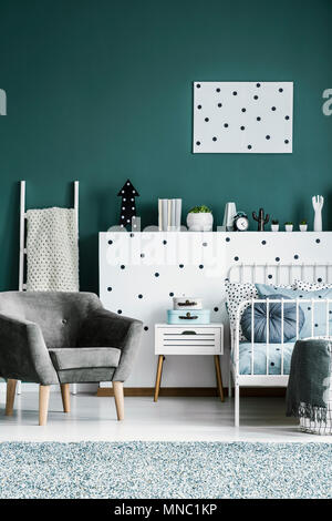 Fauteuil en daim gris à côté de lit et le cabinet au second chambre intérieur avec poster sur mur vert Banque D'Images