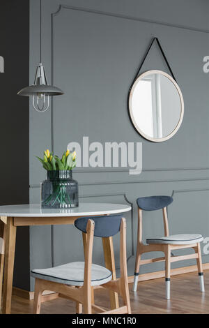 Miroir rond sur un mur gris et table en bois avec des chaises dans un coin repas Banque D'Images