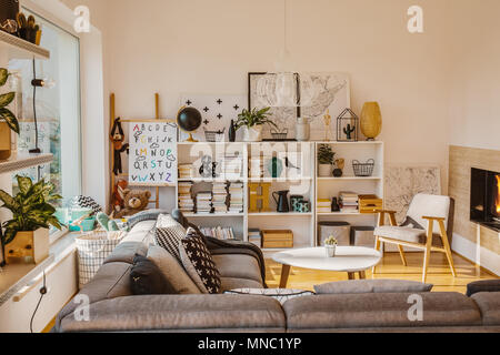 Soleil à travers une grande fenêtre en un chaleureux salon scandinave, intérieur avec une cheminée, des livres, des décorations et des jouets Banque D'Images