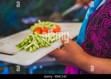 Les légumes crus et prête pour la cuisson sur une planche avec une tenue de la main d'une femme. Banque D'Images