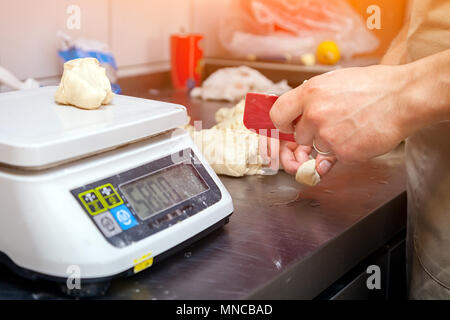 Un close-up of baker pèse sur les balances de cuisine la pâte pour la cuisson des brioches sur une table nouée avec un rouleau à pâtisserie Banque D'Images