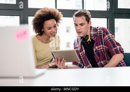 Deux jeunes employés regarder une vidéo sur Tablet PC au bureau Banque D'Images