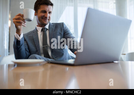 Happy young businessman using laptop et le café au bureau. Male executive working on laptop durant la pause-café. Banque D'Images