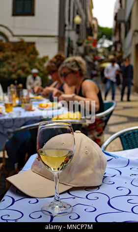 Les touristes manger dans un café dans la ville de Funchal à Madère avec un verre de vin blanc et une casquette de baseball d'un navire de croisière qui suggère les jours fériés Banque D'Images