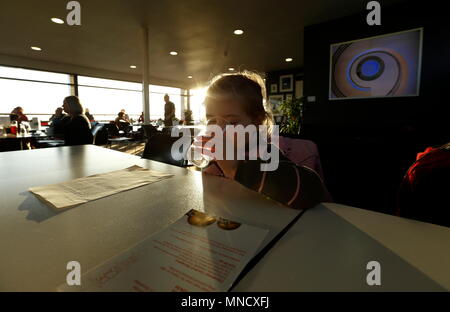 Londres, ANGLETERRE - 29 novembre : un jeune enfant de l'eau et la silhouette du sips illuminée par le soleil couchant dans les conversations avec les gens dans le café de la De La Warr Pavilion au coucher du soleil. Bexhill-on-Sea, East Sussex le 29 novembre 2015. United Kingdom. Banque D'Images