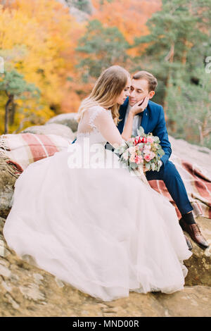 Photo verticale de les mariés assis sur les rochers. L'épouse, c'est de caresser la joue de l'époux. Banque D'Images