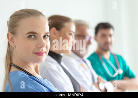 Confident female doctor looking at camera et souriant alors que ses collègues debout dans une rangée derrière elle. Une équipe expérimentée de médecins hautement qualifiés Banque D'Images