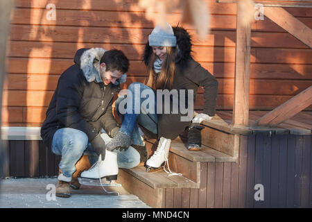 L'homme accroupi tout en aidant la femme heureuse de porter des patins à glace sur les mesures Banque D'Images