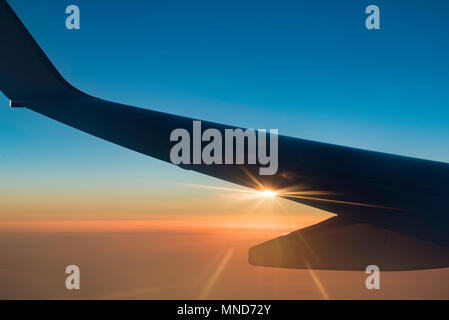 Silhouette de l'aile d'un Boeing 737 qui vole en altitude avec le soleil couchant sur le bord de l'aile Banque D'Images