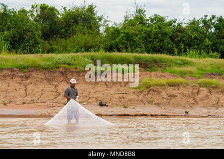 À la berge de la rivière Siem Reap, un pêcheur local avec un bouchon est debout dans l'eau brunâtre et tirant son filet de pêche. Prises en mai 2009. Banque D'Images