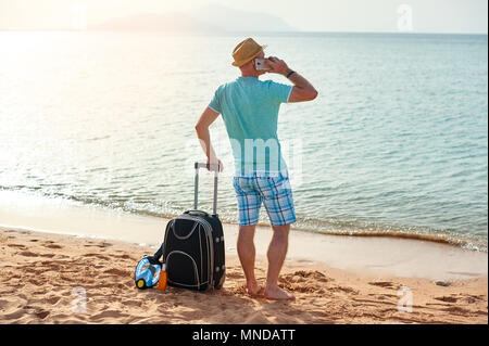 Portrait de l'homme heureux avec valise et téléphone mobile standing on beach indépendant sur une journée ensoleillée sur locations Banque D'Images