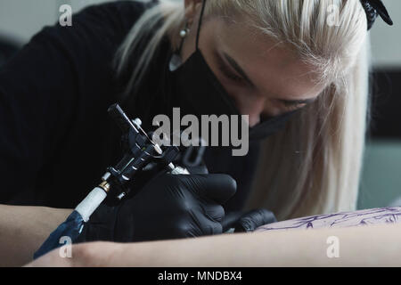 Close-up of female artist wearing mask le tatouage sur la cuisse de femme avec machine à tatouer Banque D'Images