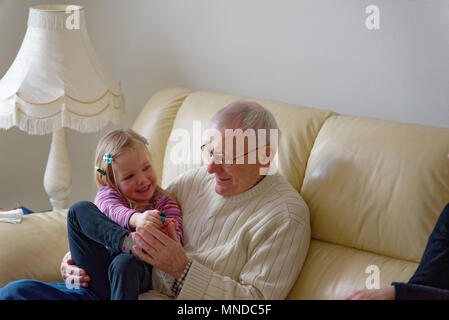 Grand-père et de ses trois ans, petite-fille rire ensemble assis sur un canapé Banque D'Images