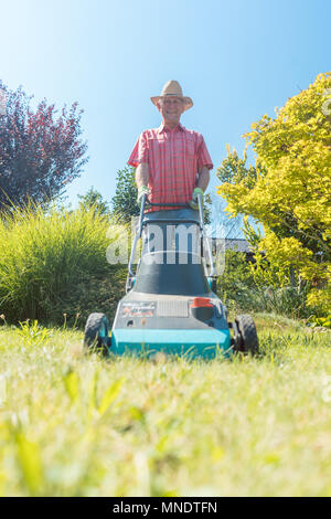 Senior man smiling pendant l'utilisation d'une machine à couper l'herbe dans le jardin Banque D'Images