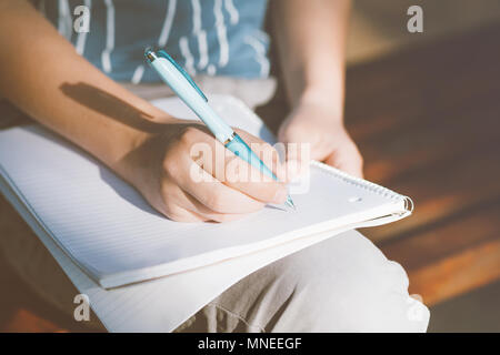 Vue en gros plan sur les mains du garçon dans l'écriture en plein air de l'ordinateur portable. Adolescent assis sur un banc en bois et faire ses devoirs. Banque D'Images