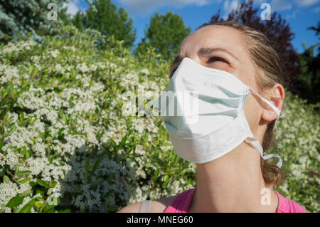 Jeune femme avec masque de protection à blooming park avec des yeux mi-clos à cause de la forte bien Banque D'Images