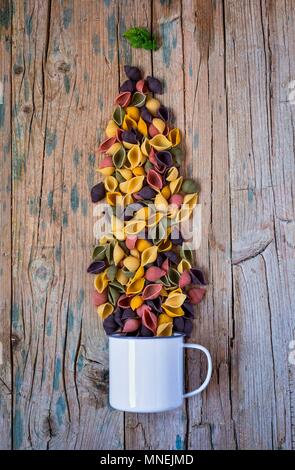 Pâtes colorées avec une tasse d'émail sur une table en bois Banque D'Images