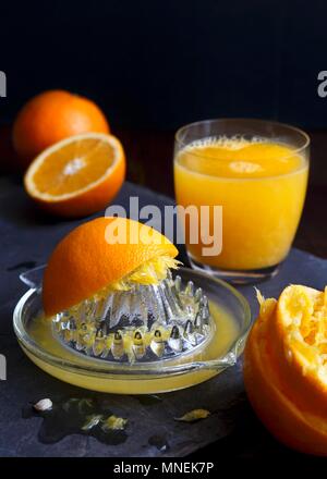 Juicet avec extracteur manuel verre pressé des oranges et un verre de jus d'orange sur une ardoise foncé Banque D'Images