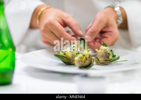 Un chef organise des artichauts marinés sur une plaque Banque D'Images