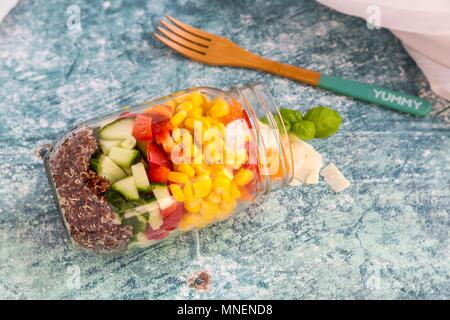 Une salade colorée dans un bocal en verre avec le quinoa rouge, concombre, poivrons, maïs, tomates, fromage pecorino et de basilic, avec une fourche en bois Banque D'Images