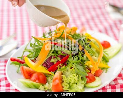 On verse la vinaigrette sur une salade mixte avec rocket, poivrons et tomates Banque D'Images