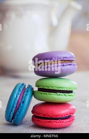 Divers différentes couleurs de macarons empilés devant une théière Banque D'Images