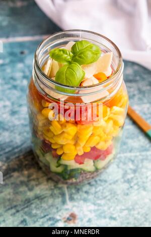 Une salade colorée dans un bocal en verre avec le quinoa rouge, concombre, poivrons, maïs, tomates, fromage pecorino et basilic Banque D'Images