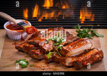 Côtes levées barbecue sur une planche en bois en face d'un incendie Banque D'Images