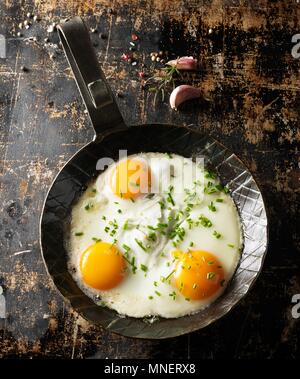 Trois oeufs au plat avec la ciboulette dans une casserole chaude, noir Banque D'Images