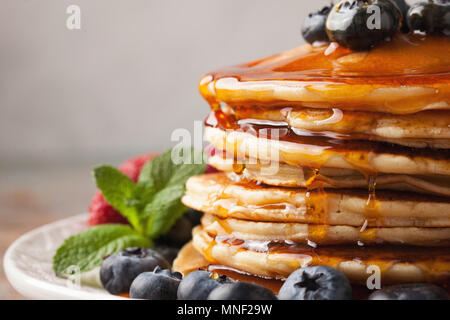 Close-up de délicieuses crêpes, avec des bleuets frais, fraises et sirop d'érable sur un fond clair. Le sirop sucré s'écoule à partir d'une pile de crêpes Banque D'Images