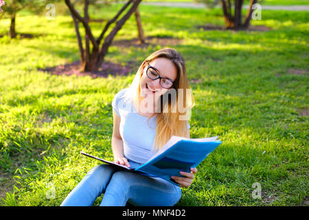 Femmes positives student sitting on Green grass in park et la lecture de l'article. Banque D'Images